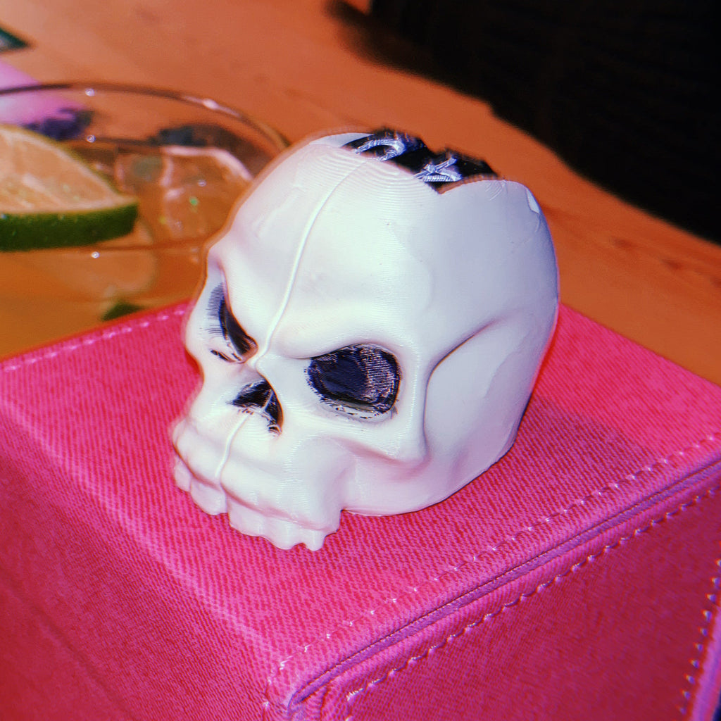 White skull life counter on a pink box with drinks and cards in the background